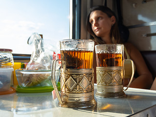 Image showing On the table in the compartment of the train are glasses with tea in metal cup holders, in the background the girl looks out the window