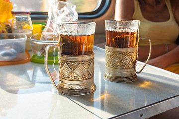 Image showing On the table in the train compartment are glasses with tea in metal cup holders.