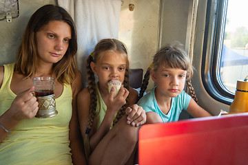 Image showing Mom and two girls are looking at the laptop screen in the train car, having a bite while