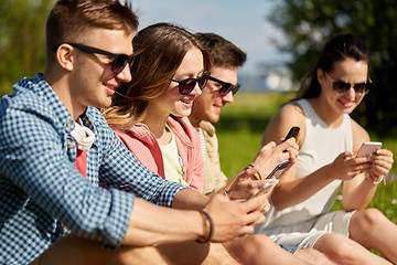Image showing smiling friends with smartphones sitting on grass