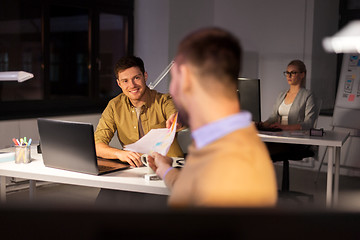 Image showing man giving papers to colleague at night office