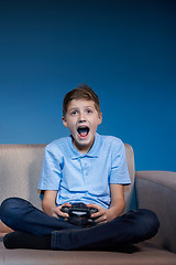 Image showing Computer game competition. Gaming concept. Excited boy sitting on sofa playing video game