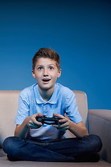 Image showing Computer game competition. Gaming concept. Boy sitting on sofa playing video game with joystick