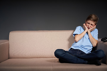 Image showing Tired boy sitting on the sofa holding head in hands