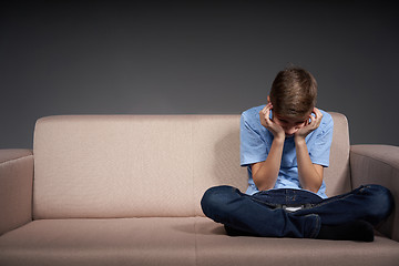 Image showing Tired boy sitting on the sofa holding head in hands