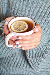 Image showing Female hands holding mug of hot tea with lemon in morning.