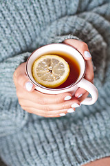 Image showing Female hands holding mug of hot tea with lemon in morning.