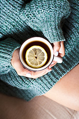 Image showing Female hands holding mug of hot tea with lemon in morning.