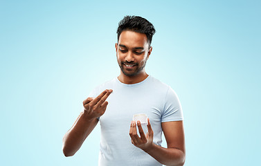 Image showing happy indian man applying cream to face