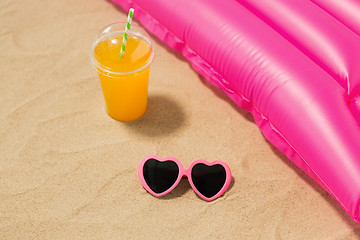 Image showing sunglasses, juice and pool mattress on beach sand