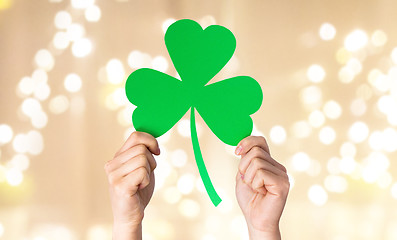 Image showing hands holding green shamrock over festive lights