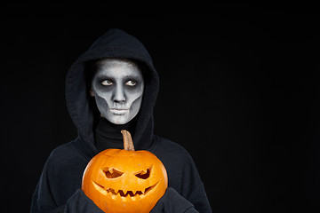 Image showing Boy with Halloween makeup holding Jack O\'Lantern pumpkin on black background