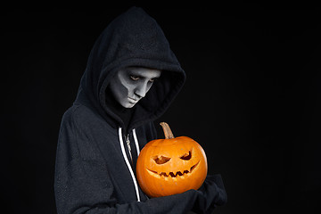 Image showing Boy with Halloween makeup holding Jack O\'Lantern pumpkin on black background