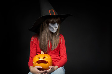 Image showing Serious Halloween witch holding Jack O\'Lantern pumpkin looking at camera