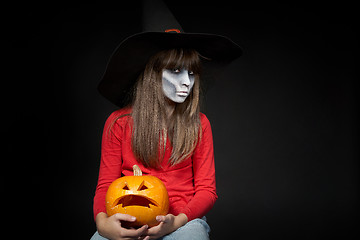 Image showing Serious Halloween witch holding Jack O\'Lantern pumpkin looking at camera