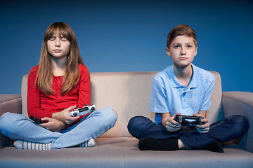 Image showing Children sitting on sofa playing video game with joysticks