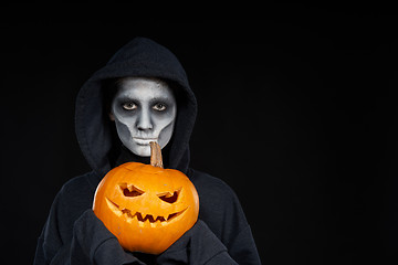 Image showing Boy with Halloween makeup holding Jack O\'Lantern pumpkin on black background