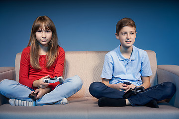 Image showing Children sitting on sofa playing video game with joysticks