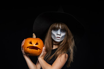 Image showing Serious Halloween witch holding Jack-O-Lantern pumpkin looking at camera