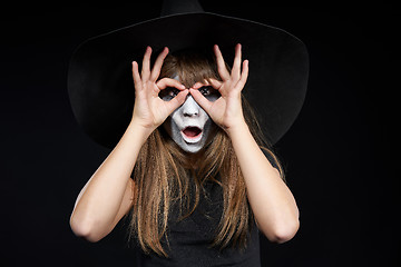 Image showing Closeup of Halloween witch girl looking at camera through fingers making binoculars