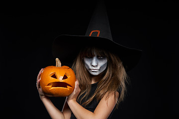 Image showing Serious Halloween witch holding Jack-O-Lantern pumpkin looking at camera