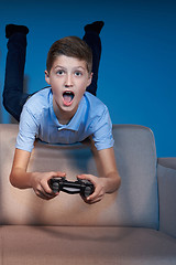 Image showing Excited boy lying on sofa back playing video game with joystick