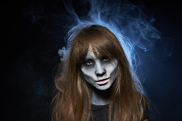 Image showing A girl with zombie makeup over dark background with smoke and backlight