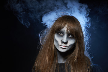 Image showing A girl with zombie makeup over dark background with smoke and backlight