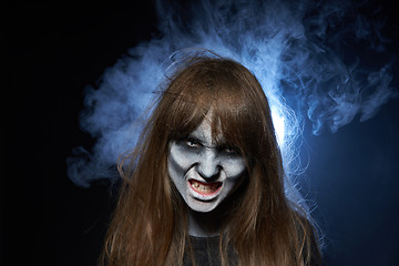 Image showing A girl with zombie makeup over dark background with smoke and backlight