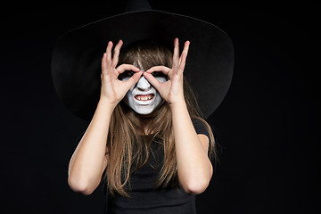 Image showing Closeup of Halloween witch girl looking at camera through fingers making binoculars