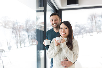 Image showing multiethnic couple enjoying morning coffee by the window