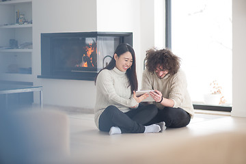 Image showing multiethnic couple using tablet computer in front of fireplace