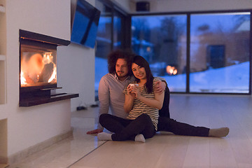 Image showing happy multiethnic couple sitting in front of fireplace