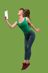 Image showing Image of young woman over green background using laptop computer or tablet gadget while jumping.