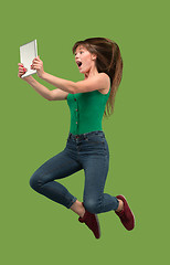 Image showing Image of young woman over green background using laptop computer or tablet gadget while jumping.