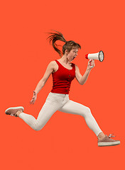 Image showing Beautiful young woman jumping with megaphone isolated over red background