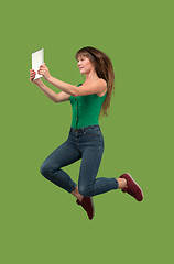 Image showing Image of young woman over green background using laptop computer or tablet gadget while jumping.