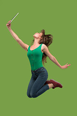 Image showing Image of young woman over green background using laptop computer or tablet gadget while jumping.