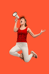 Image showing Beautiful young woman jumping with megaphone isolated over red background