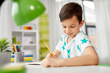 Image showing happy boy writing or drawing to notebook at home