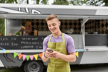 Image showing salesman in apron with smartphone at food truck