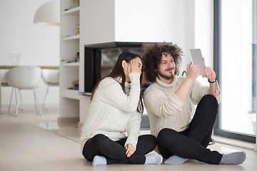 Image showing multiethnic couple using tablet computer in front of fireplace