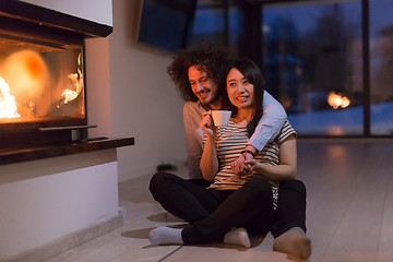 Image showing happy multiethnic couple sitting in front of fireplace