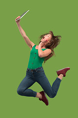 Image showing Image of young woman over green background using laptop computer or tablet gadget while jumping.