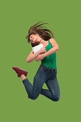 Image showing Image of young woman over green background using laptop computer or tablet gadget while jumping.