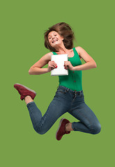 Image showing Image of young woman over green background using laptop computer or tablet gadget while jumping.