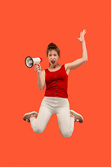 Image showing Beautiful young woman jumping with megaphone isolated over red background