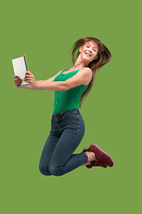 Image showing Image of young woman over green background using laptop computer or tablet gadget while jumping.