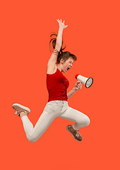 Image showing Beautiful young woman jumping with megaphone isolated over red background