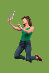 Image showing Image of young woman over green background using laptop computer or tablet gadget while jumping.